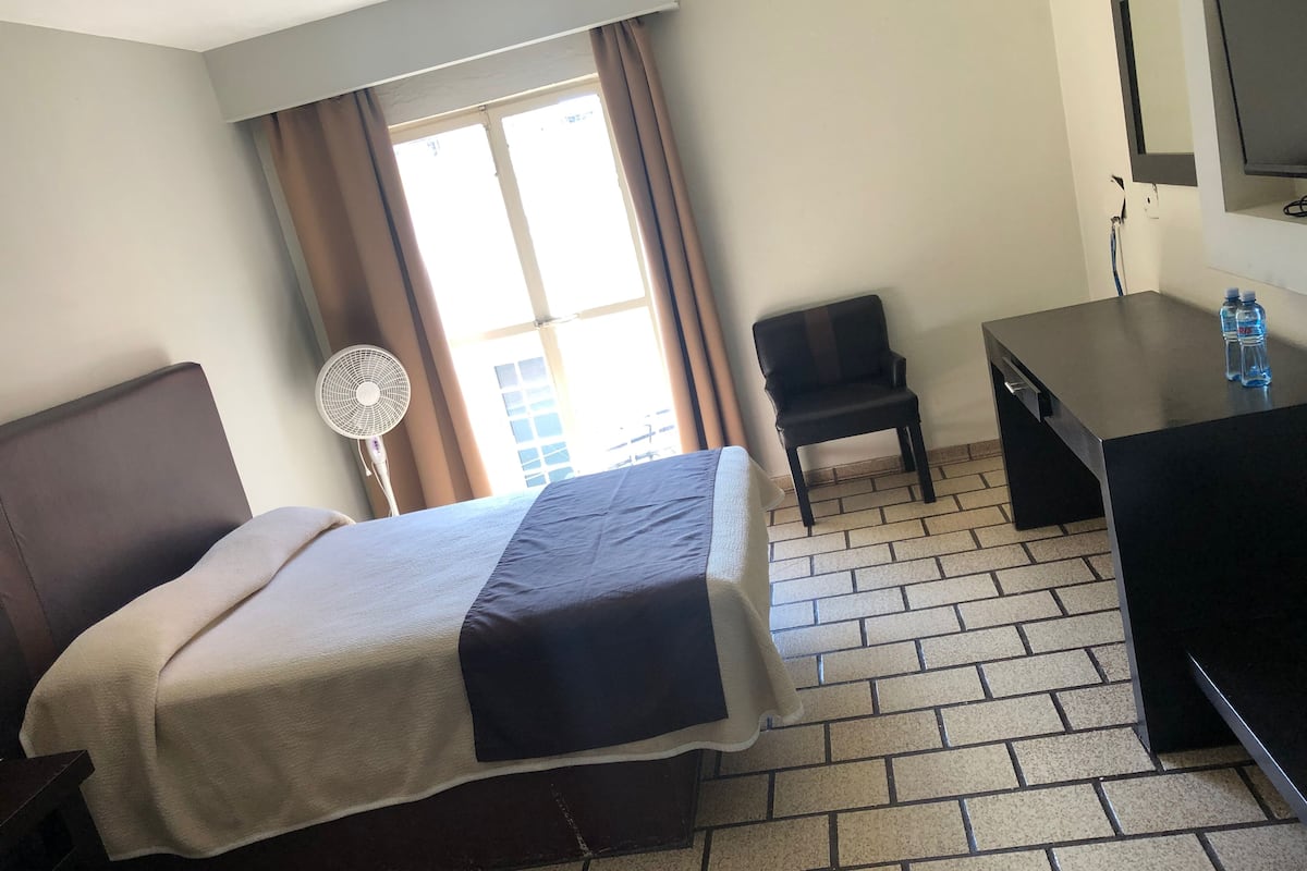 Habitación de hotel con cama, escritorio, silla, ventilador y televisor.
