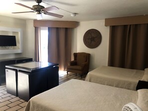 Una habitación de hotel con cama, una silla, un escritorio, televisión y ventilador de techo.