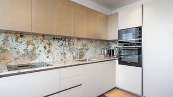 Una cuina moderna amb armaris blancs, una barra de fons de marbre, electrodomèstics d'acer inoxidable i un forn encastrat.
