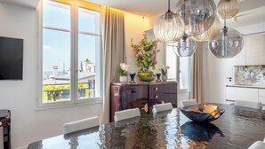 Ein moderner Essbereich mit großem Tisch, Stühlen, einem Blumenstrauß und Blick auf die Stadt durch große Fenster.
