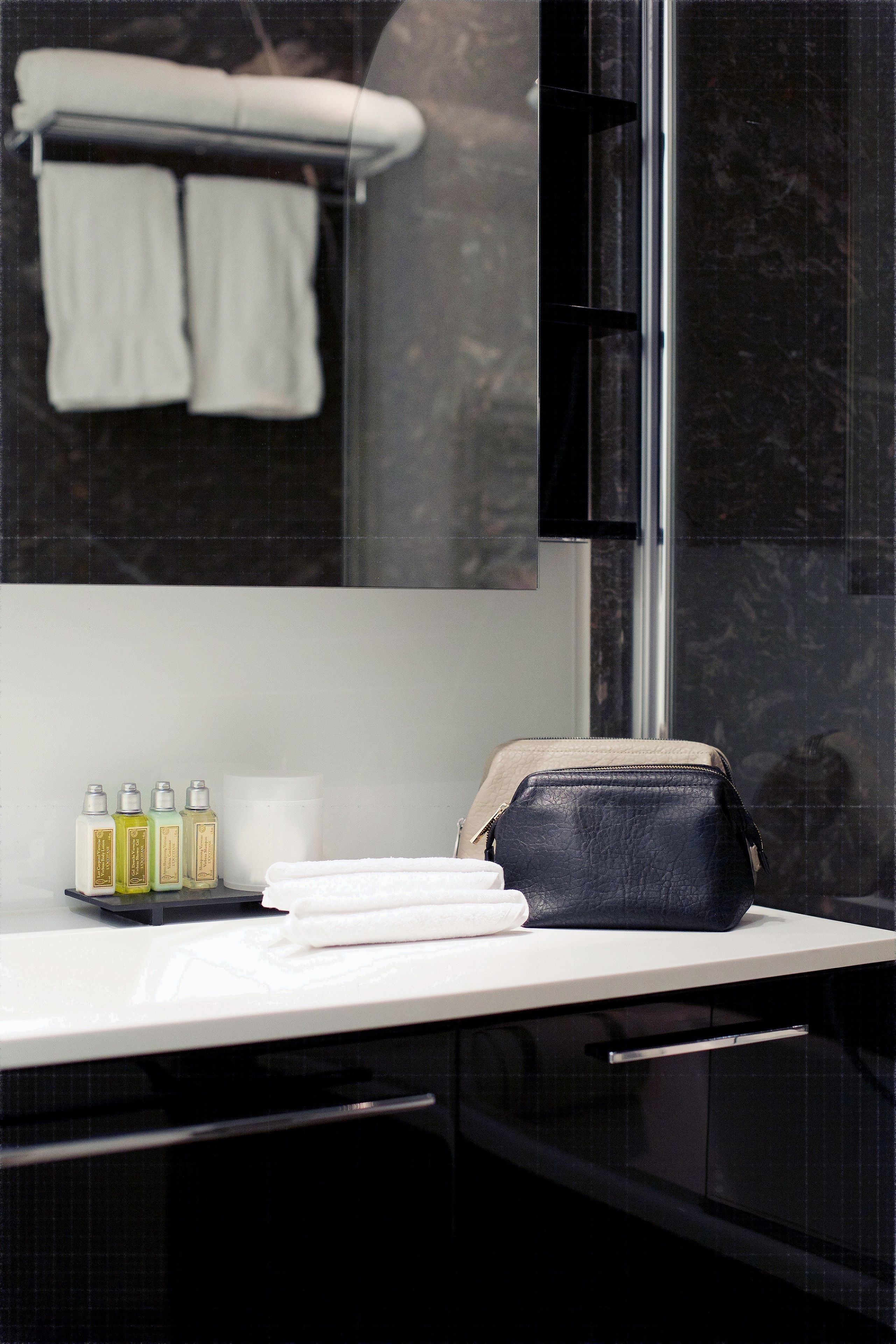 A bathroom with a white countertop, a black leather bag, and four toiletry bottles.