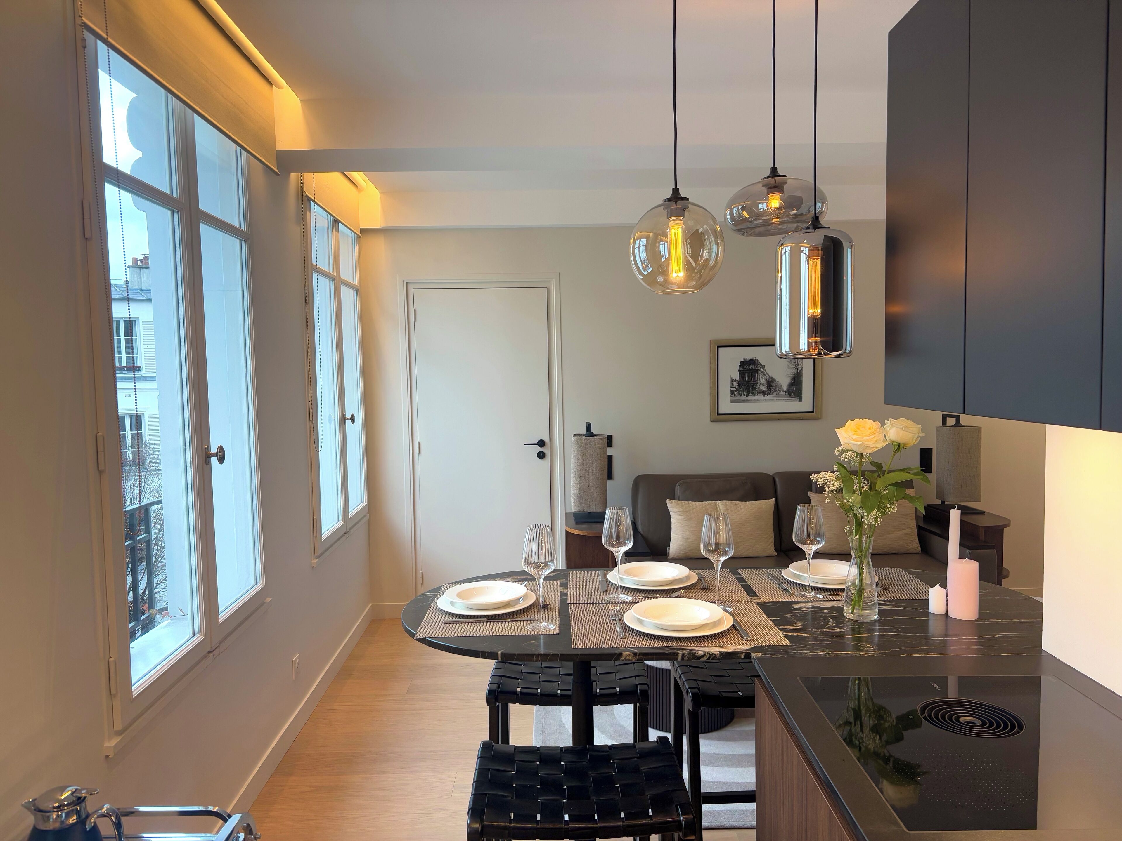 Un comedor moderno con una mesa redonda dispuesta para cuatro personas, una silla negra y una isla de cocina con encimera de vidrio.