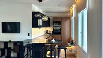 Una cocina moderna con una isla central, taburetes de bar, iluminación colgante y un amplio ventanal.