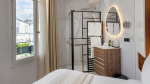 Ein modernes Badezimmer mit Duschkabine aus Glas, Holzwaschtisch, großem Spiegel und Blick auf die Stadt durch ein Fenster.