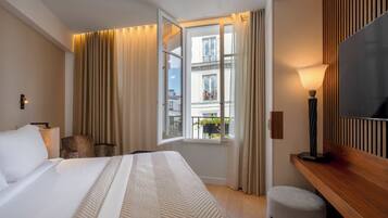 A hotel room with a bed, a desk, a chair, a TV, and a window with curtains.