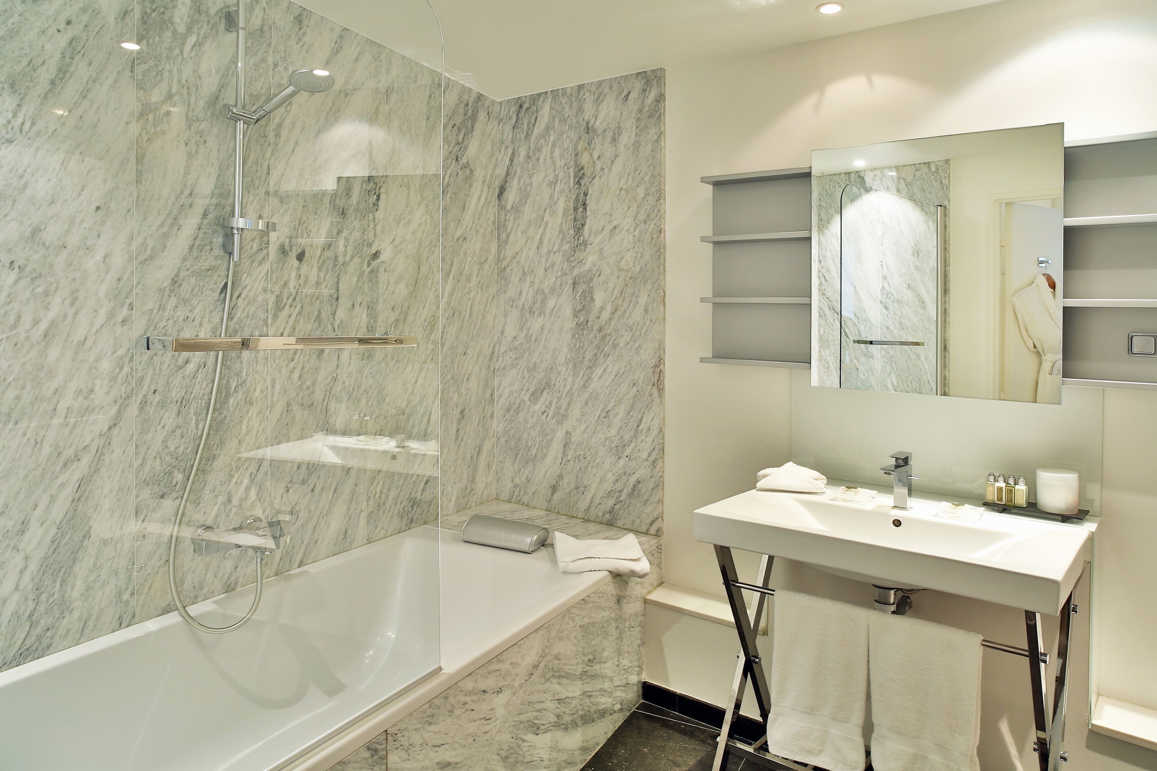 A modern bathroom with a marble shower, a white sink, and a mirror above the sink.