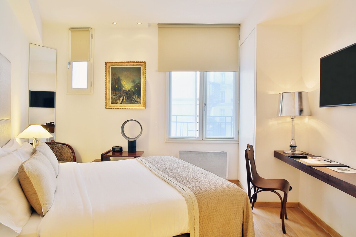 A hotel room with a bed, a desk, a chair, a television, a painting, and a window.
