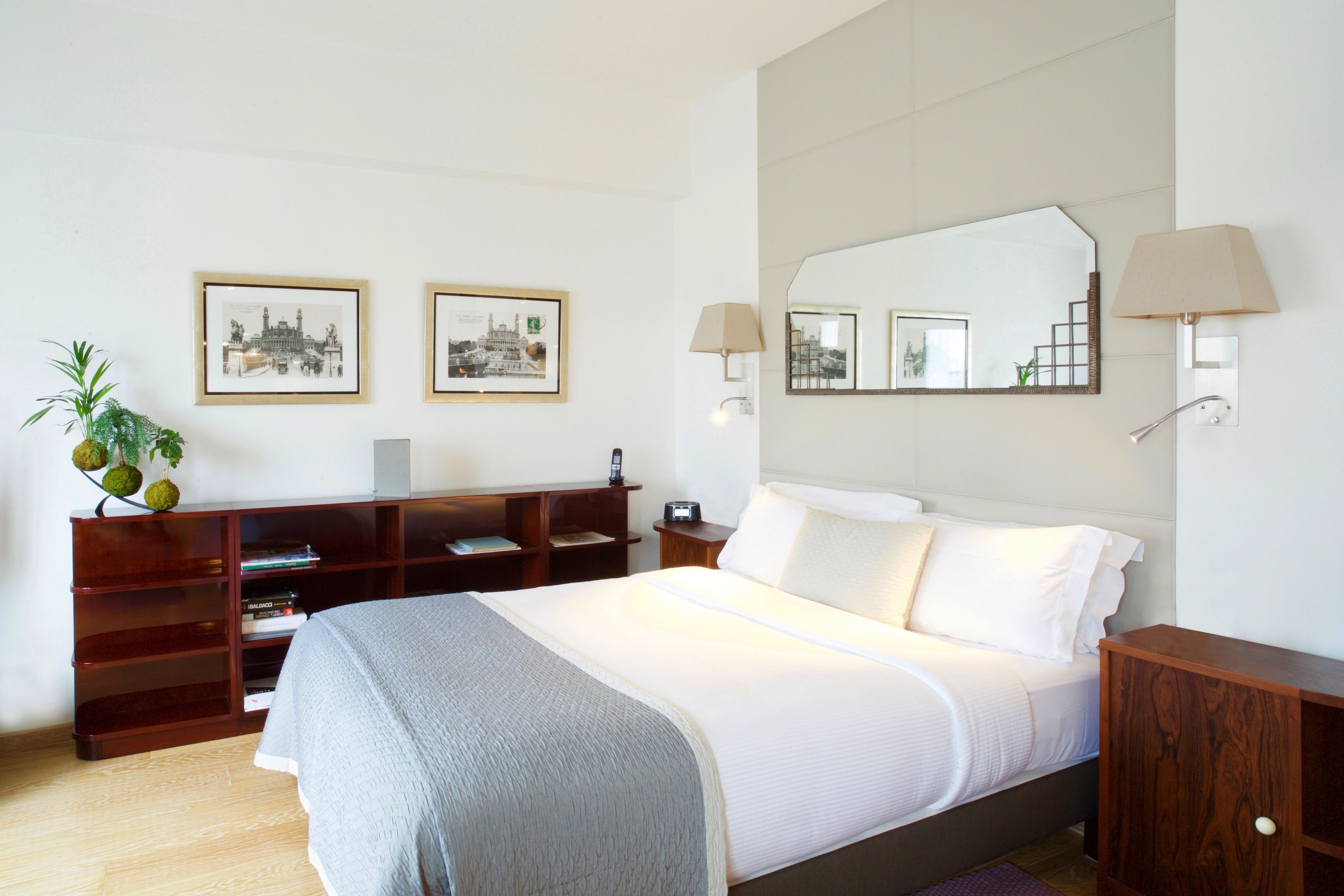 A hotel room with a large bed, a wooden nightstand, a desk with a lamp, and two framed pictures on the wall.