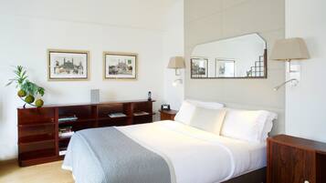 A hotel room with a large bed, a wooden nightstand, a desk with a lamp, and two framed pictures on the wall.