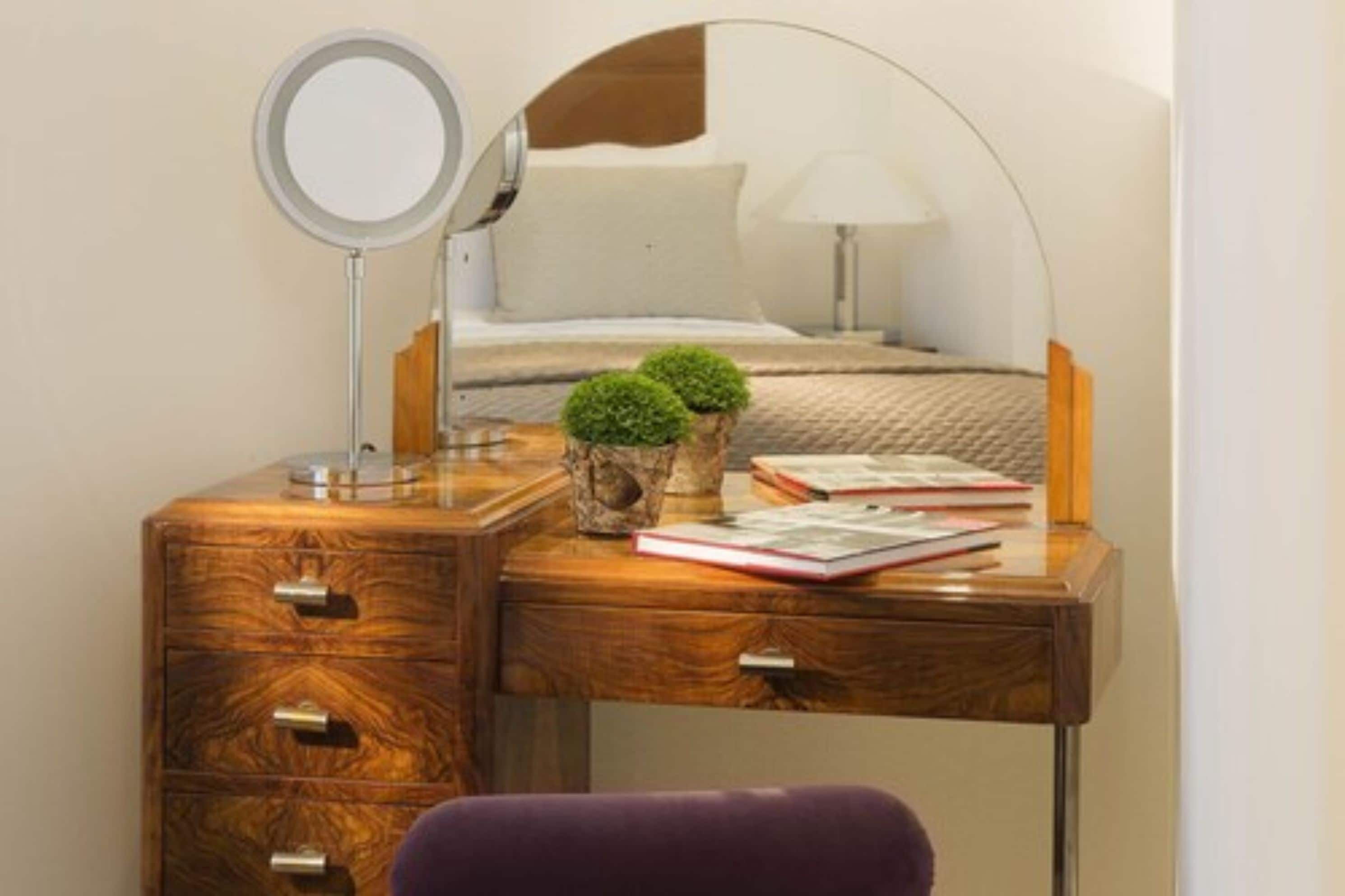 A wooden desk with a mirror, two small potted plants, and a book.