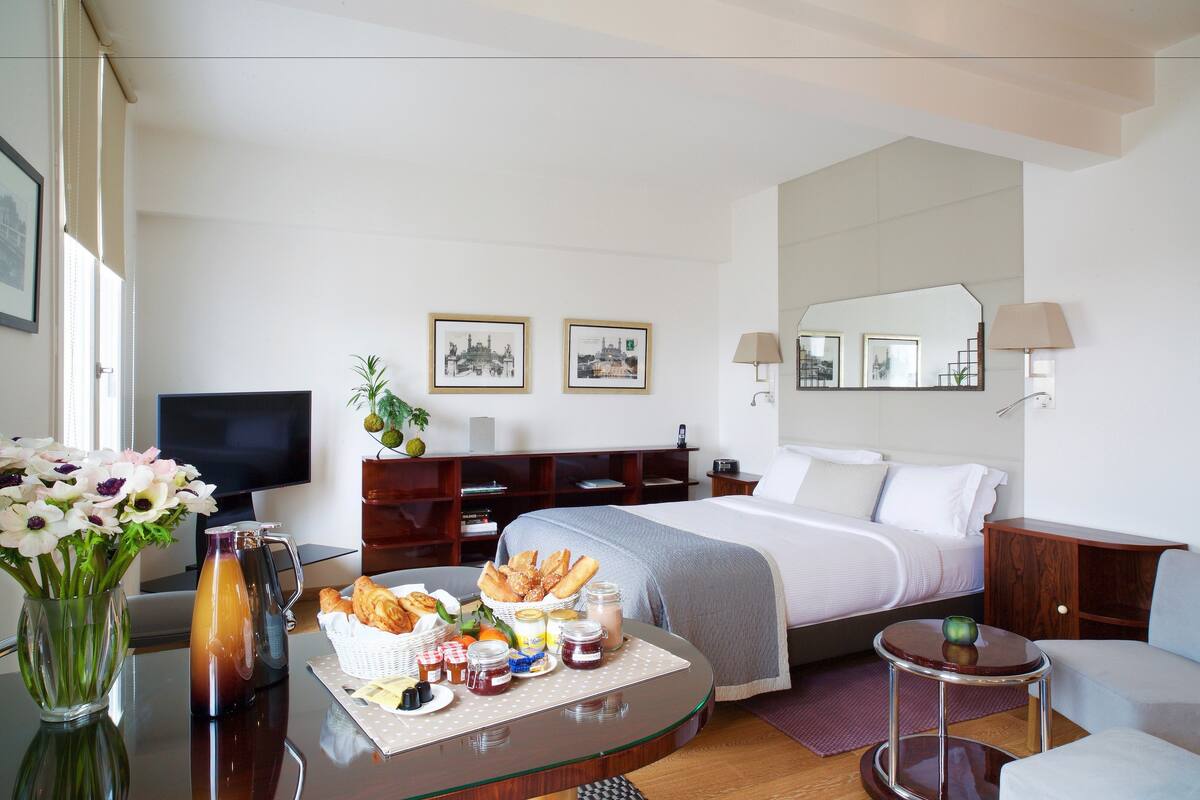 Una habitación de hotel con cama, televisión, mesa de comedor y alimentos, y un espejo.