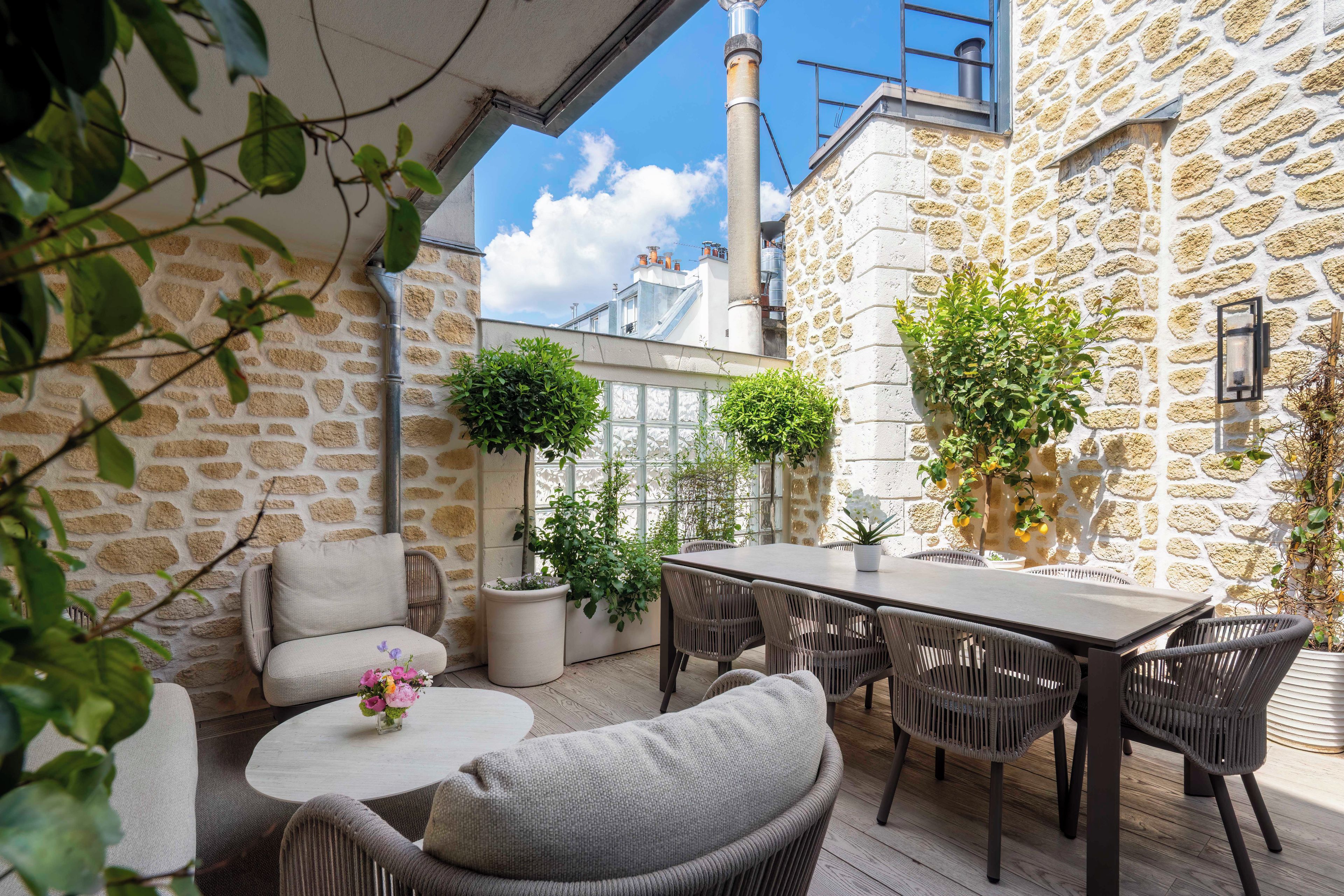 Un bâtiment en pierre doté d’un patio aménagé avec des meubles en osier, une table et des plantes en pot.