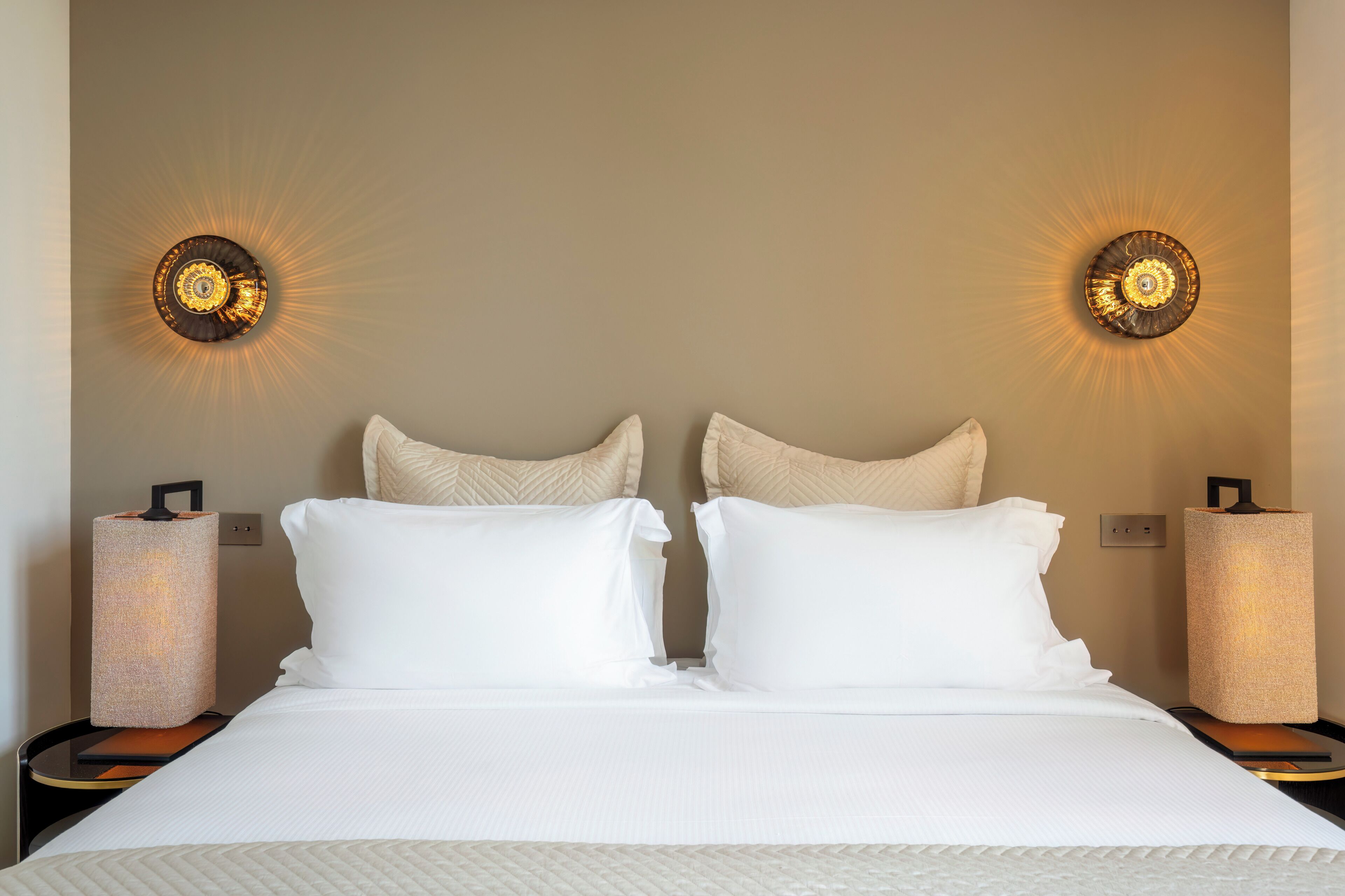 Une chambre d’hôtel avec un grand lit, deux tables de chevet et des lampes fixées au mur.