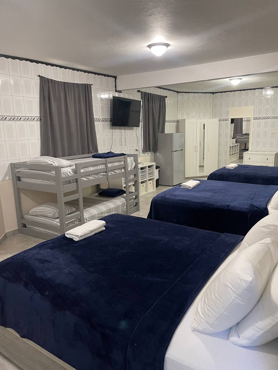 Habitación de hotel con dos camas, una litera, un televisor, un espejo y un armario.