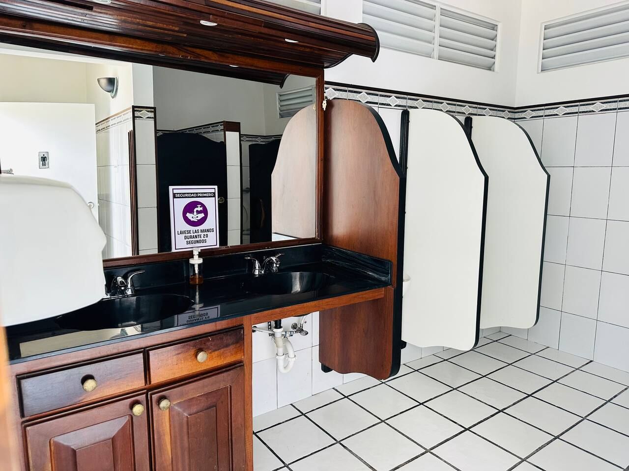 Un baño con tocador de madera, un lavamanos negro y un espejo. Hay un letrero con un círculo púrpura y texto.