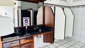 Un baño con tocador de madera, un lavamanos negro y un espejo. Hay un letrero con un círculo púrpura y texto.