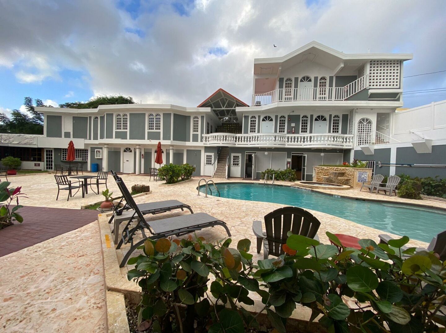 A two-story building with a swimming pool, outdoor seating, and a covered patio area.