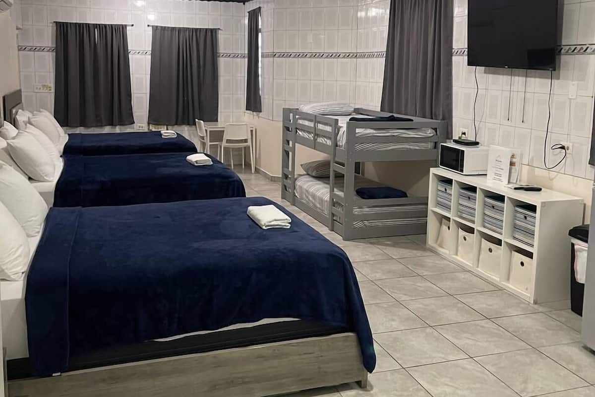 A hotel room with three beds, a bunk bed, a TV, and a desk with storage.