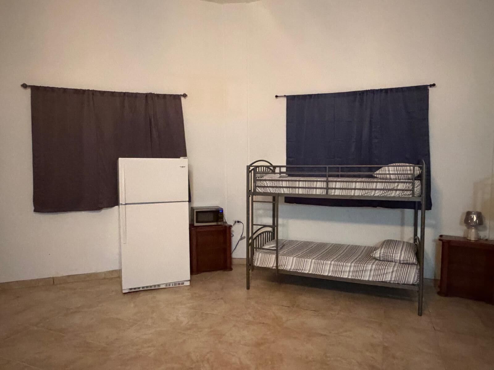 A bunk bed with a microwave on a small table, a refrigerator, and a window with curtains.