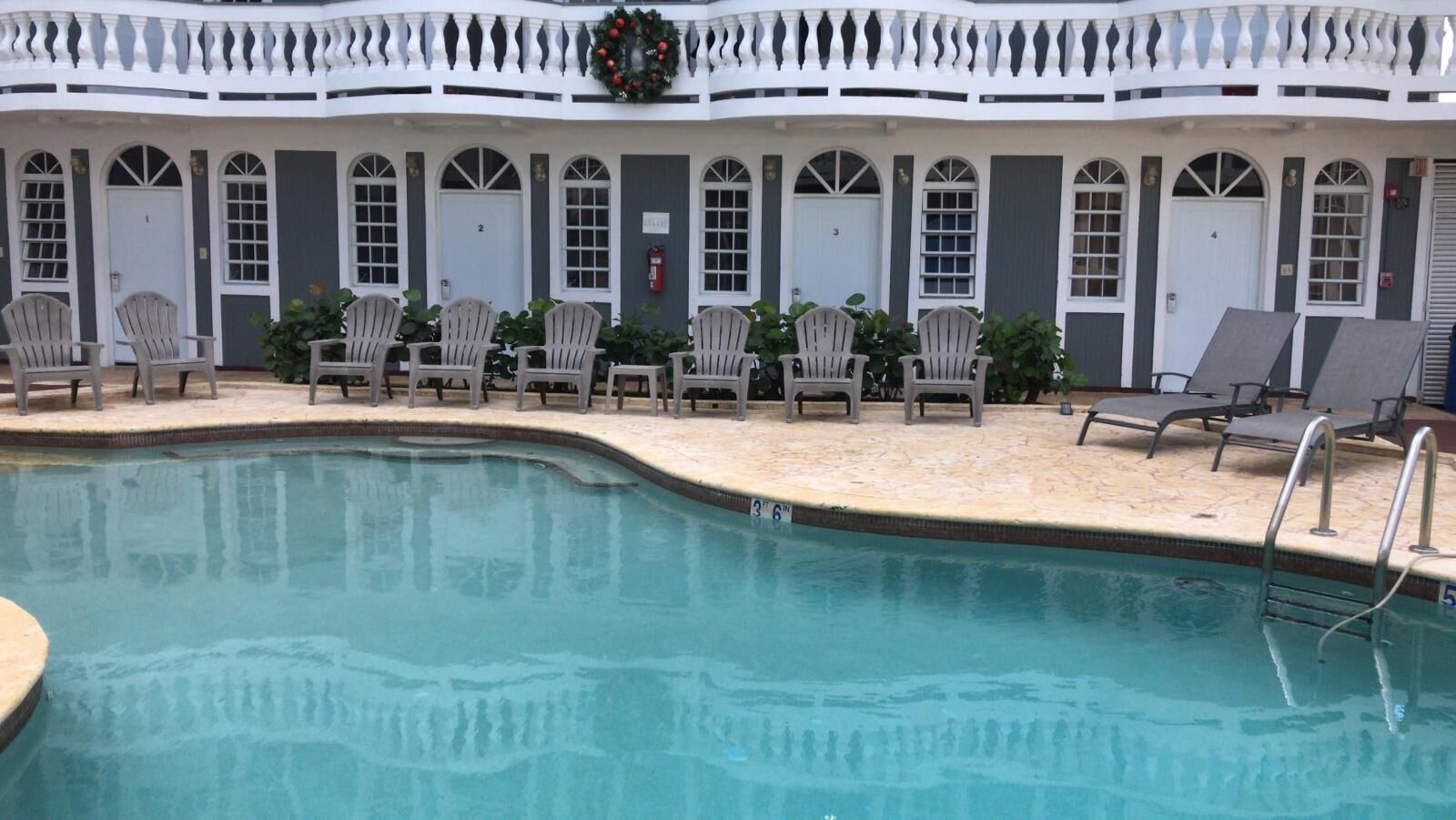 Área de piscina com espreguiçadeiras e um espaço de estar coberto com portas numeradas de 2 a 6.