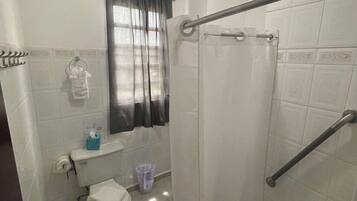 A small, clean bathroom with a toilet, a shower with a glass door, a handrail, and a toilet paper holder.