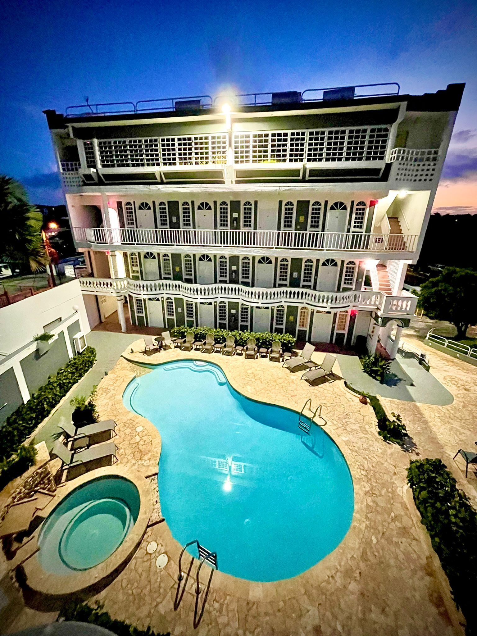 A multi-story hotel with a swimming pool, outdoor seating, and a well-lit facade.