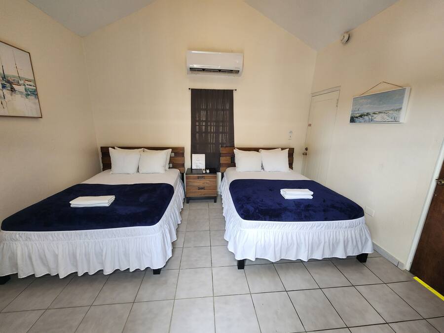 A hotel room with two beds, a nightstand, an air conditioning unit, and a door.