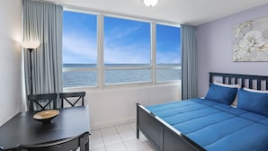 A bedroom with a bed, a table with a bowl, two chairs, a window with curtains, and a ceiling light. - Castle Beach Suites by MiaRentals (Miami Beach)