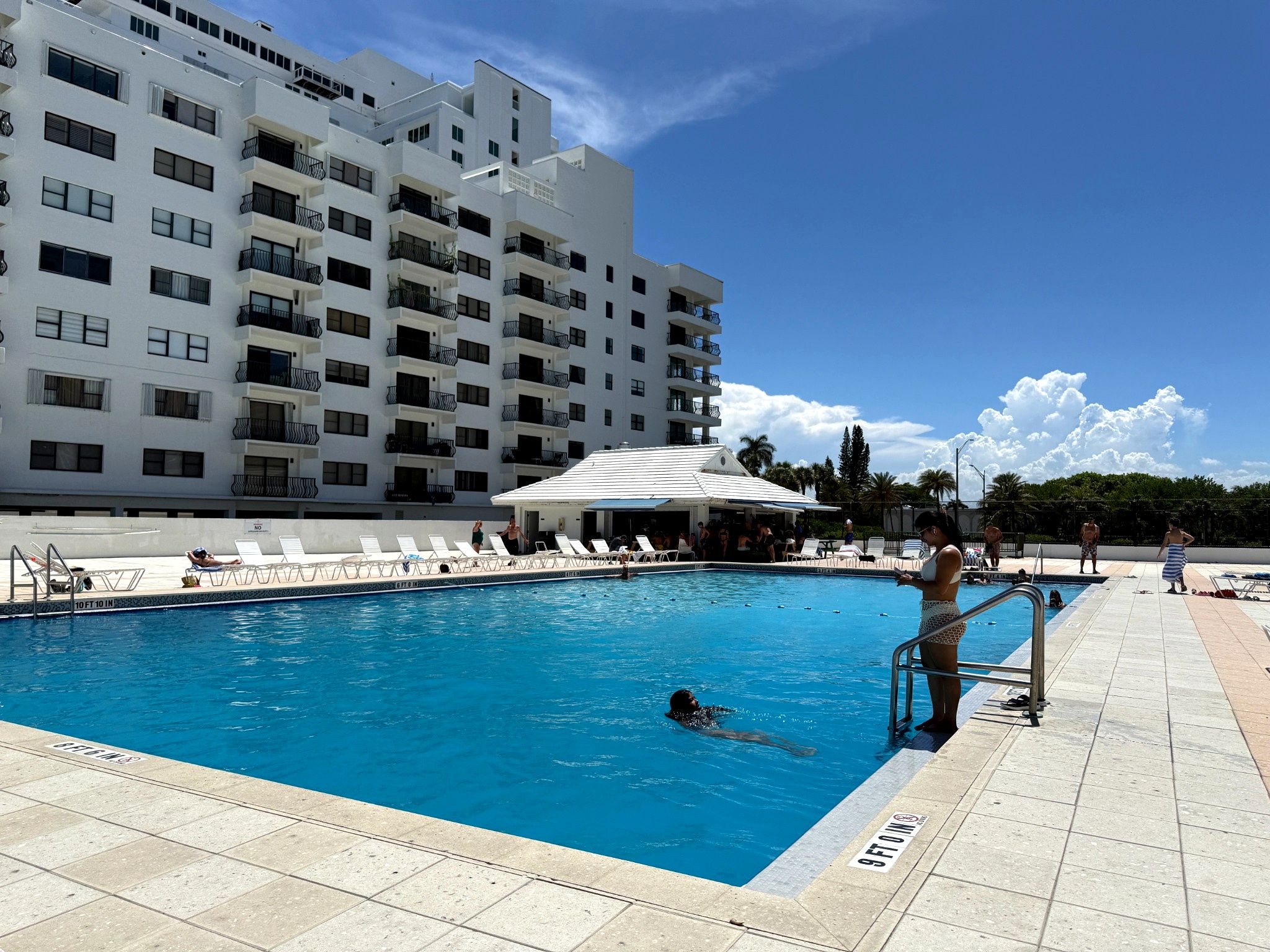 Una piscina con sillones de descanso y un edificio al fondo.