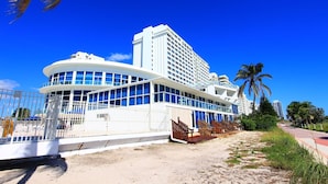 A large, modern hotel with a curved facade, multiple balconies, and a sandy beachfront setting. - Castle Beach Suites by MiaRentals (Miami Beach)
