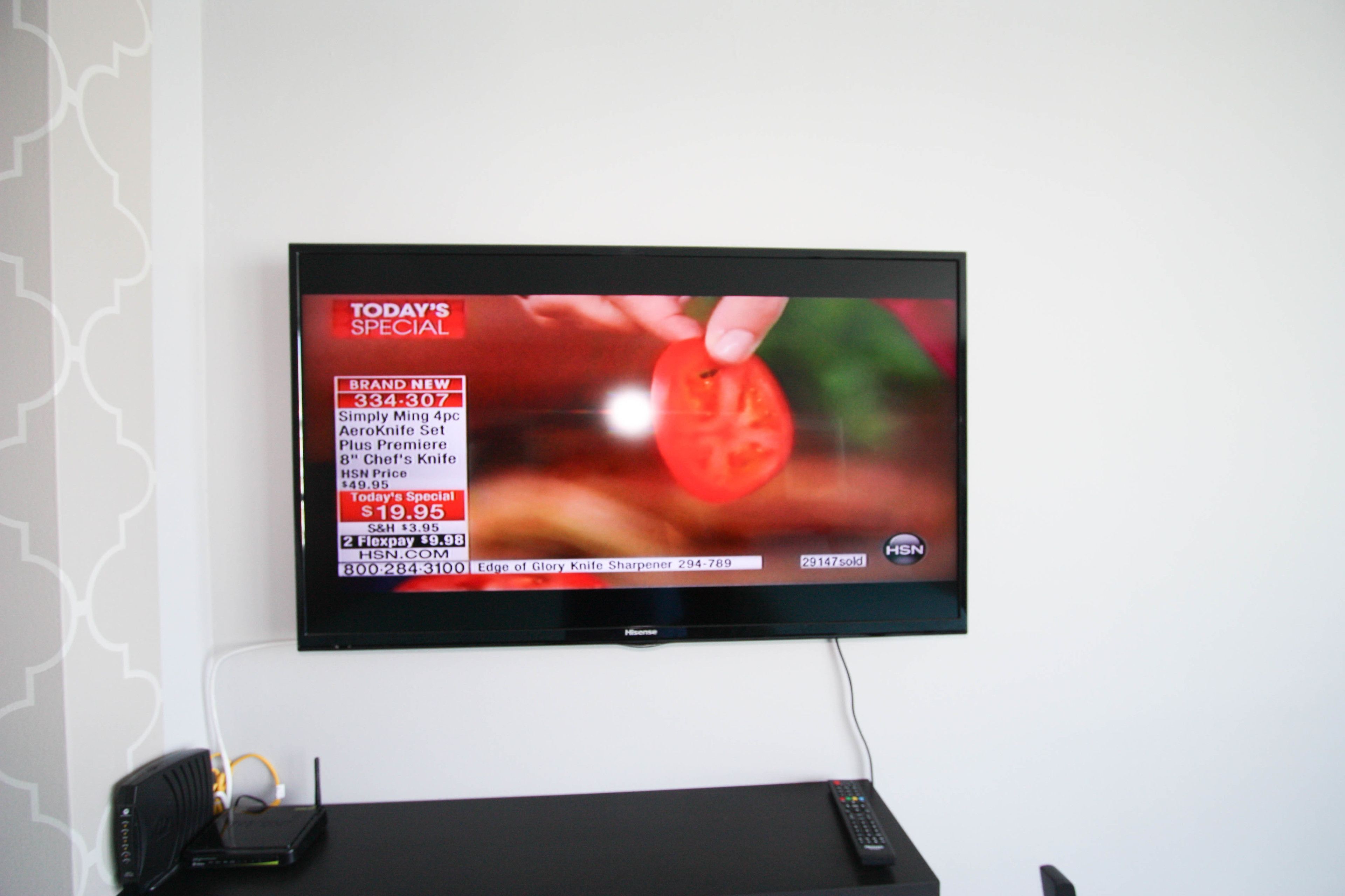 Een flatscreen televisie bevestigd aan een witte muur met behang met een patroon aan de linkerkant.
