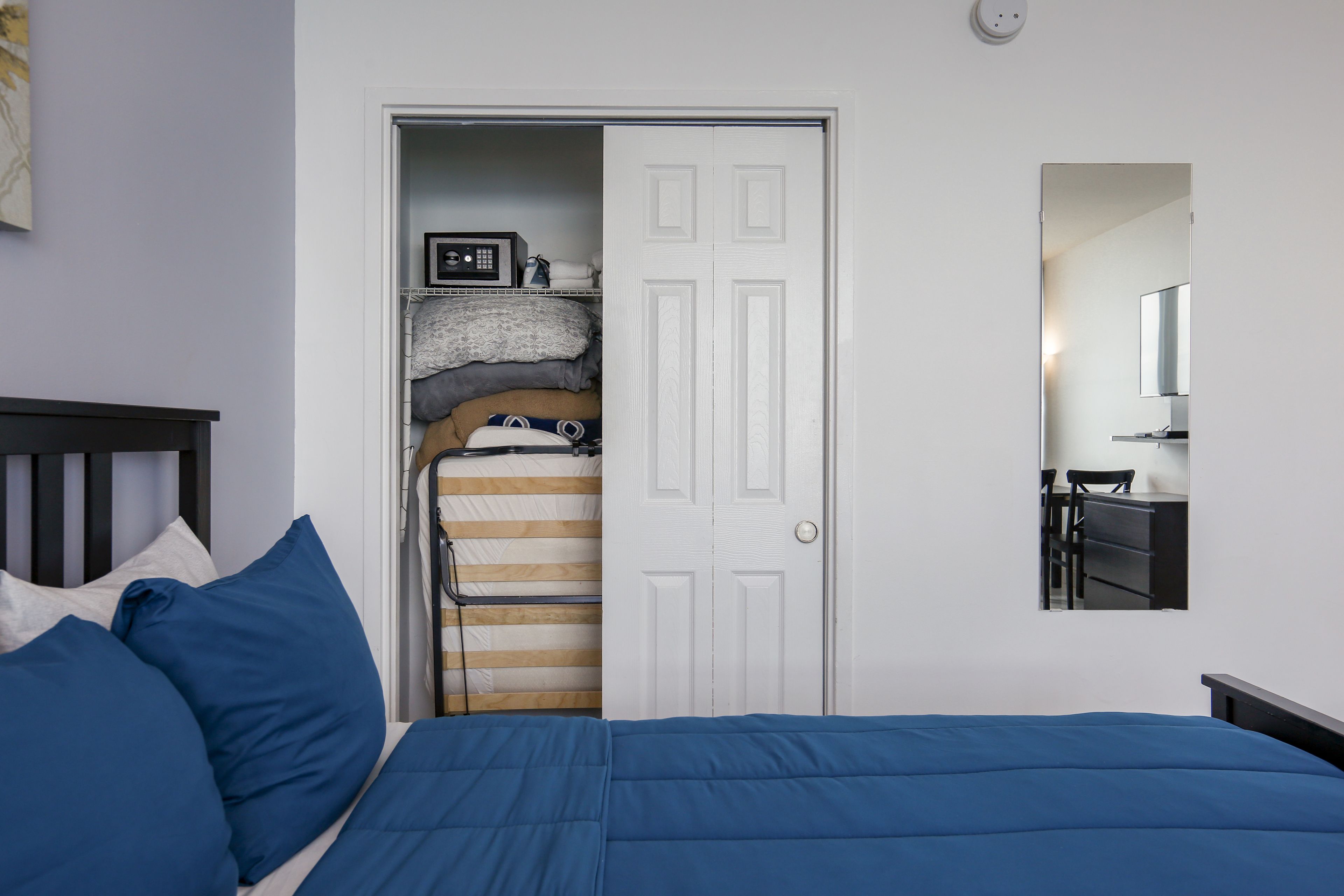 Een slaapkamer met een bed, een kledingkast, een spiegel en een klein bureau met stoel.