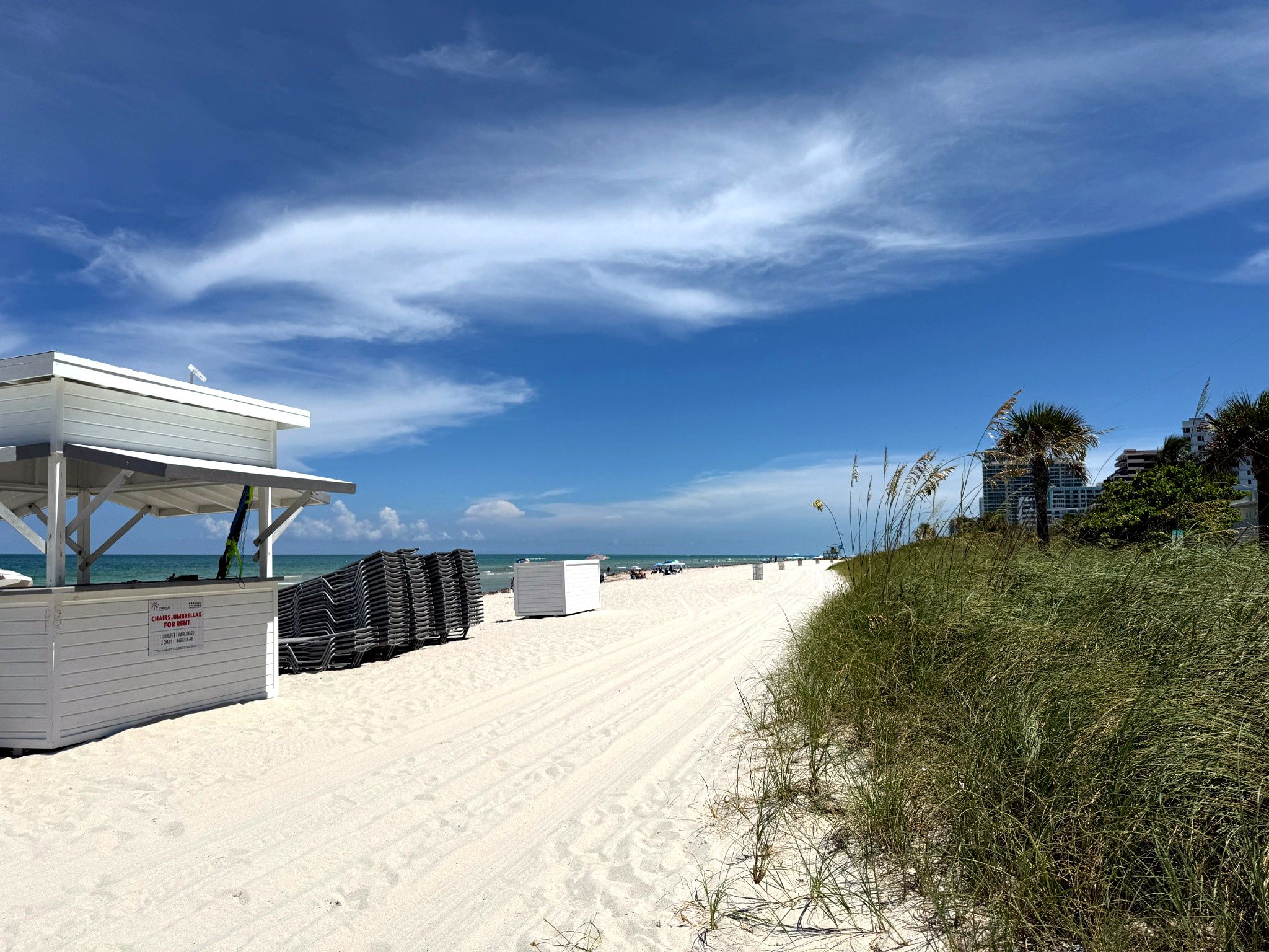 A beach with a white building, umbrellas, and chairs for rent.