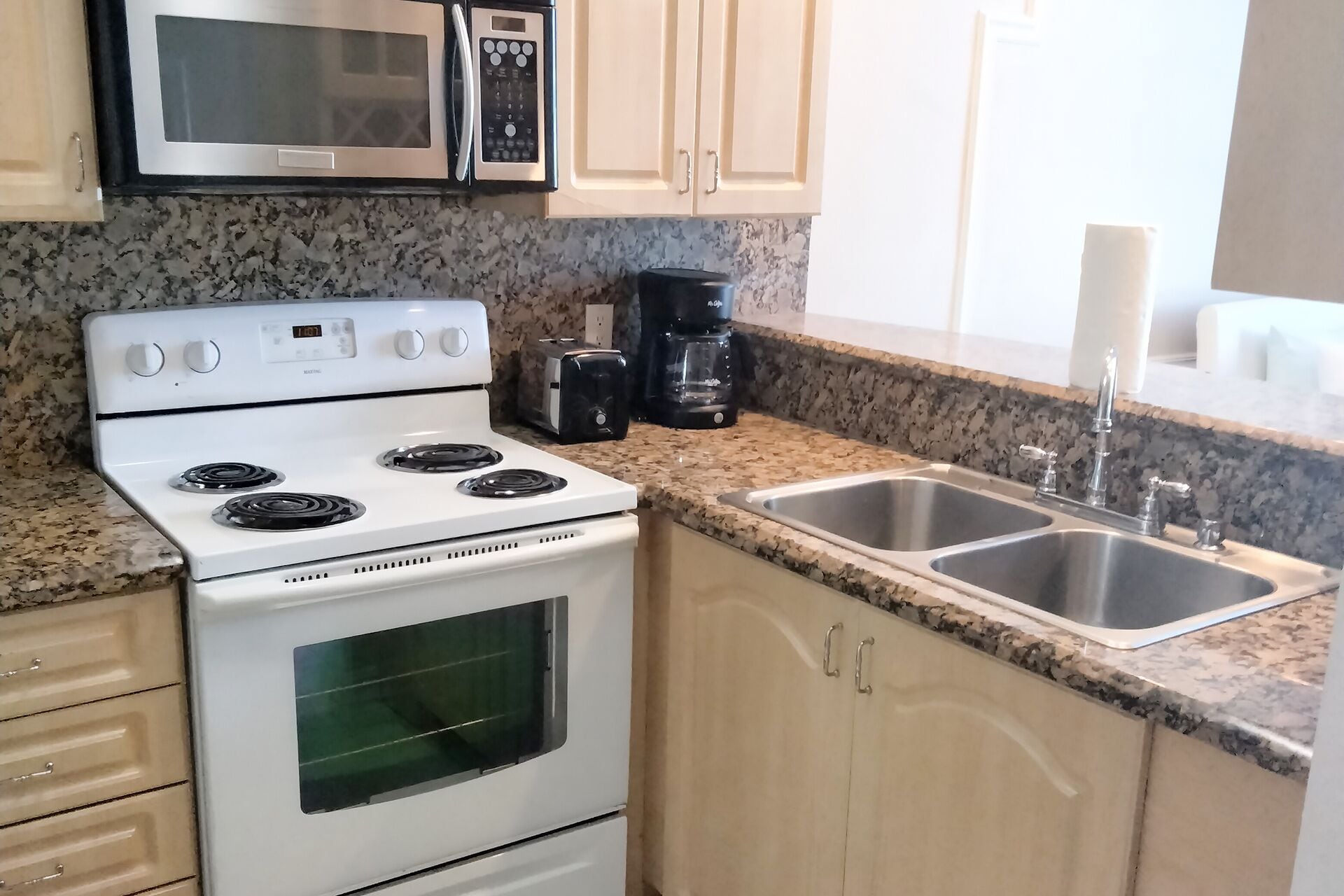A kitchen with a white stove, a microwave, a coffee maker, and a double sink.