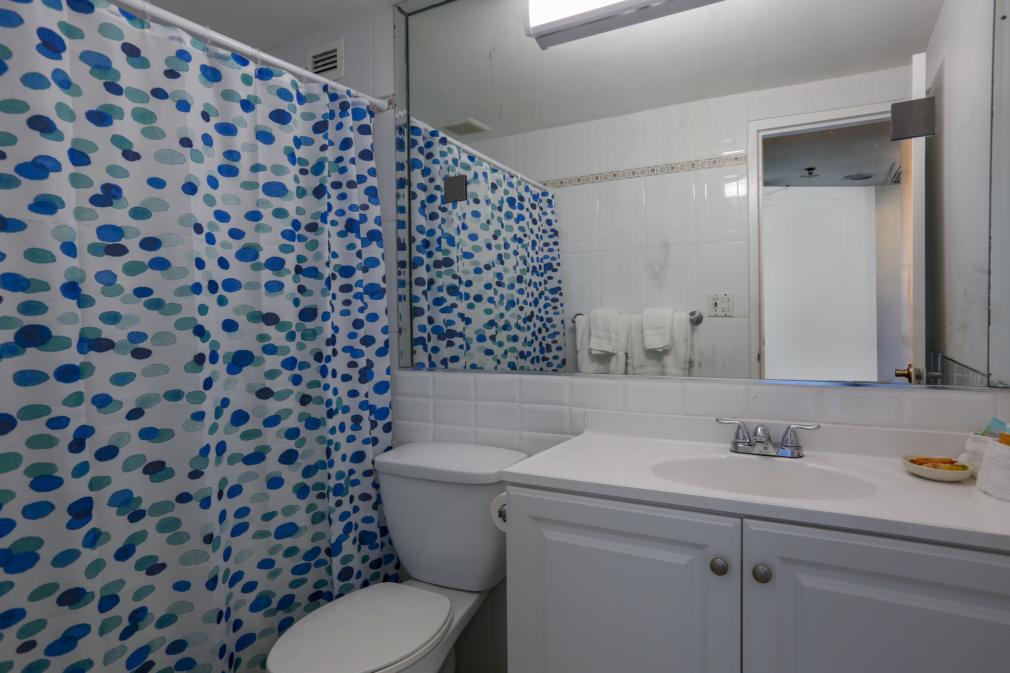 Une salle de bain avec un lavabo blanc, des toilettes et un rideau de douche à pois bleus et verts.