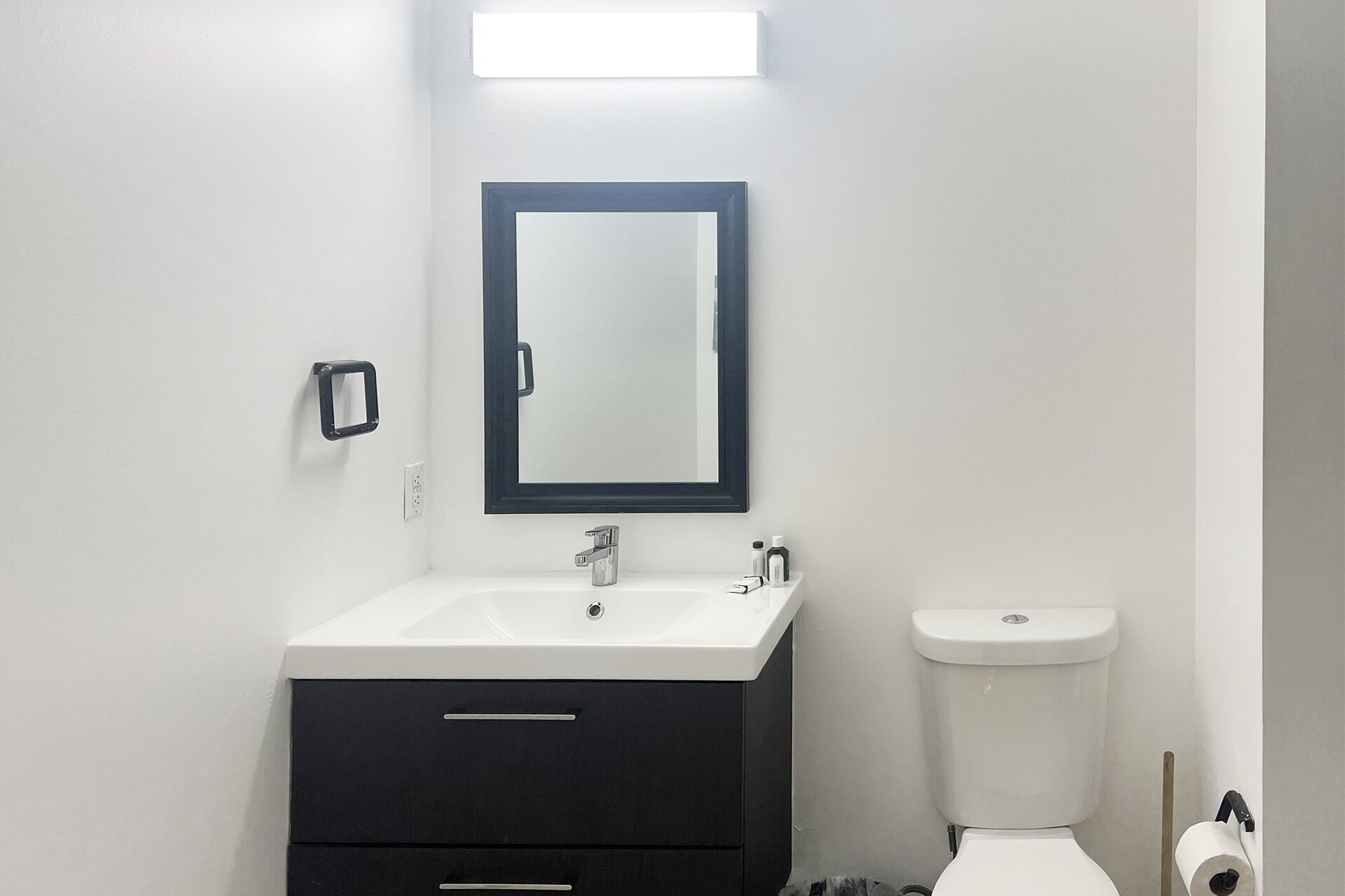 Un baño con lavamanos blanco, mueble oscuro y un inodoro.