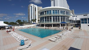 A large pool area with lounge chairs, a swimming pool, and a modern building with a curved facade. - Castle Beach Suites by MiaRentals (Miami Beach)