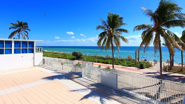 A beachside view with a white building, palm trees, and a clear blue sky. - Castle Beach Suites by MiaRentals (Miami Beach)