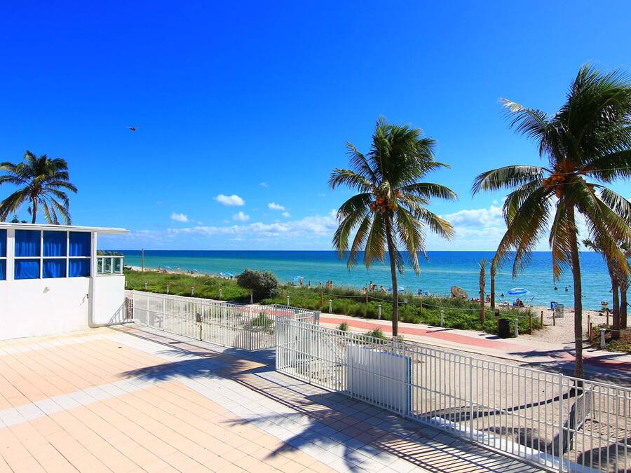 A beachside view with a white building, palm trees, and a clear blue sky.