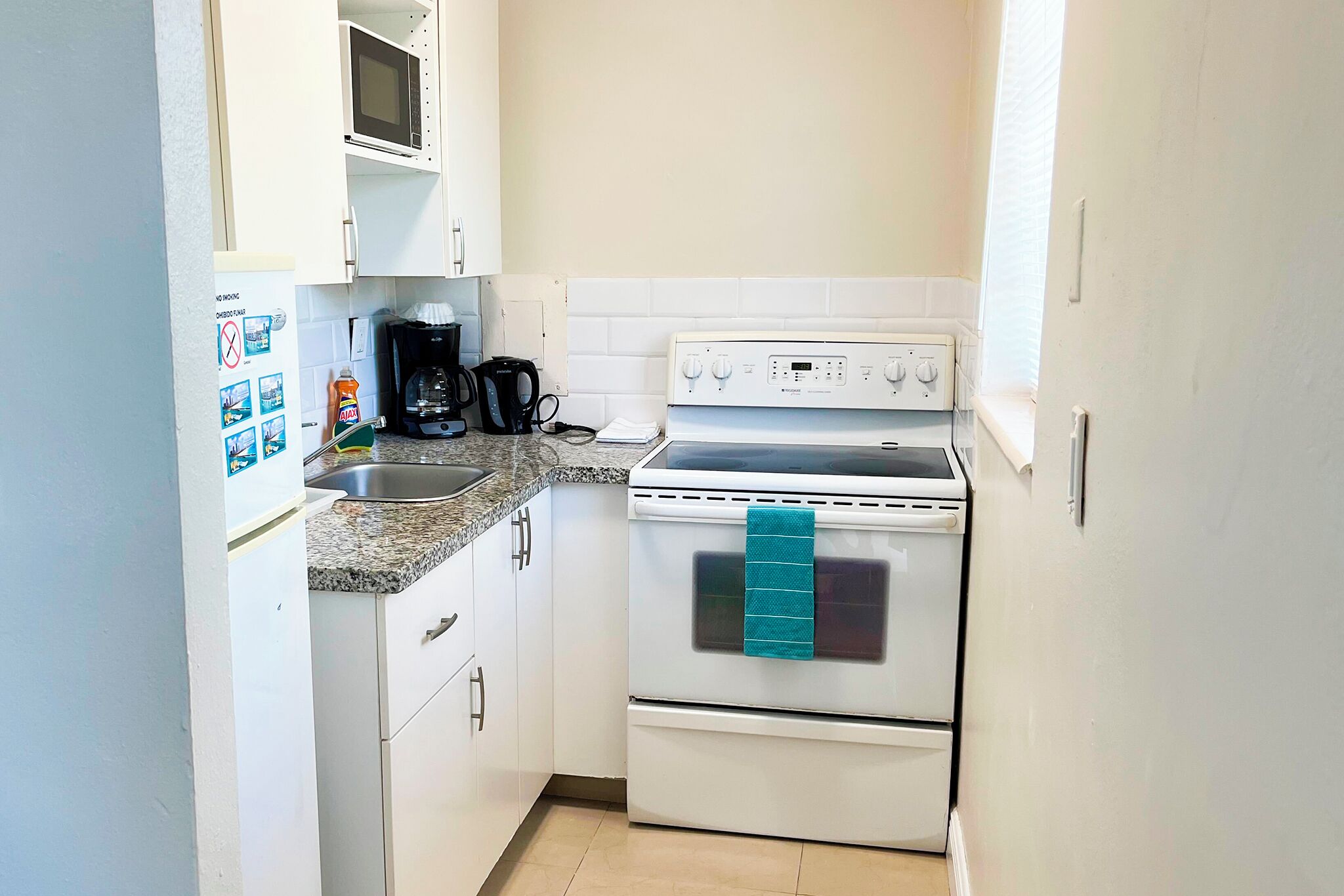 A compact kitchen with white cabinets, a microwave, a stove, and a coffee maker.