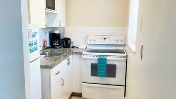 A compact kitchen with white cabinets, a microwave, a stove, and a coffee maker.