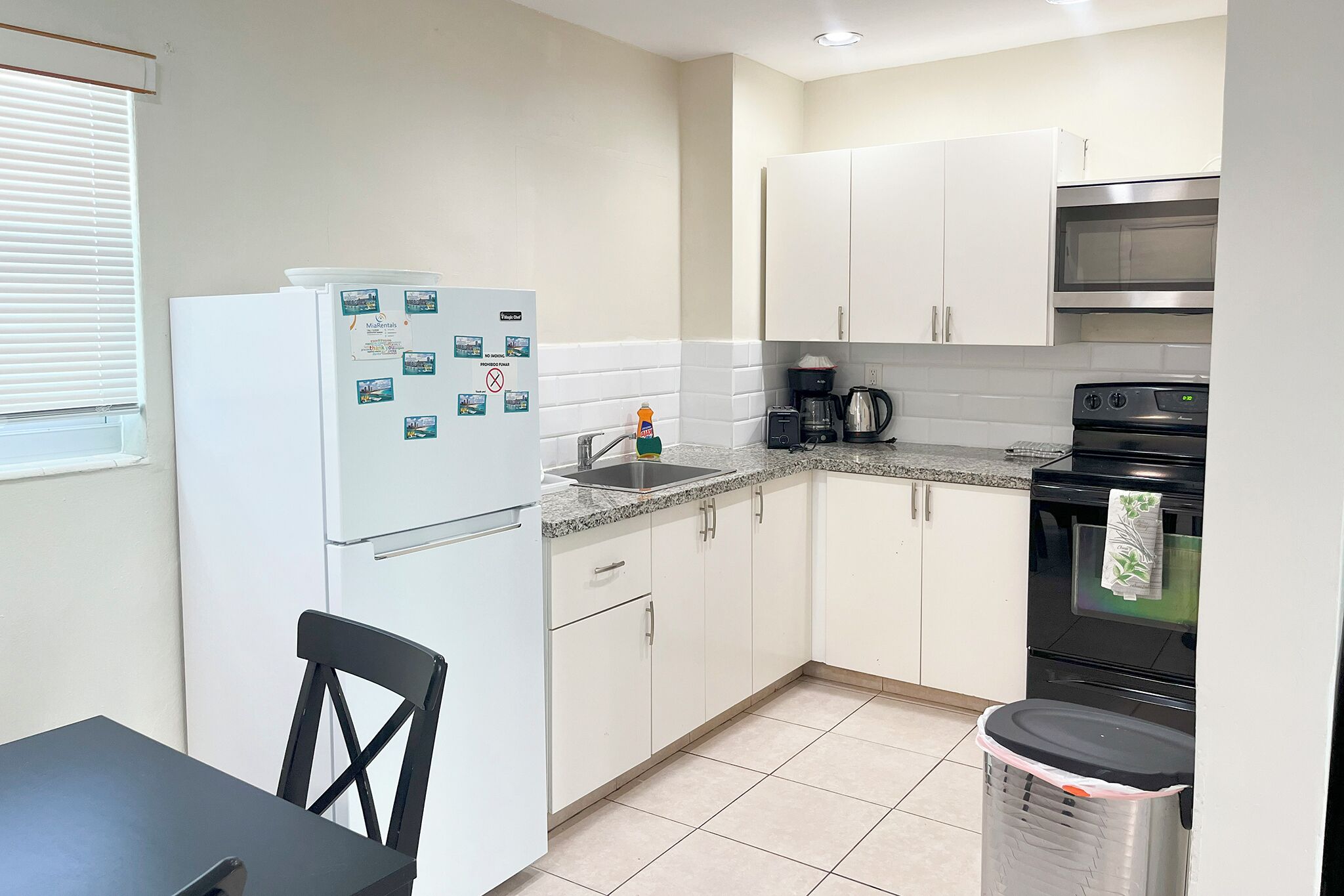A compact kitchen with white cabinets, a stainless steel oven, a coffee maker, and a trash bin.