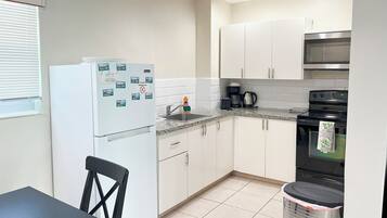 A compact kitchen with white cabinets, a stainless steel oven, a coffee maker, and a trash bin.