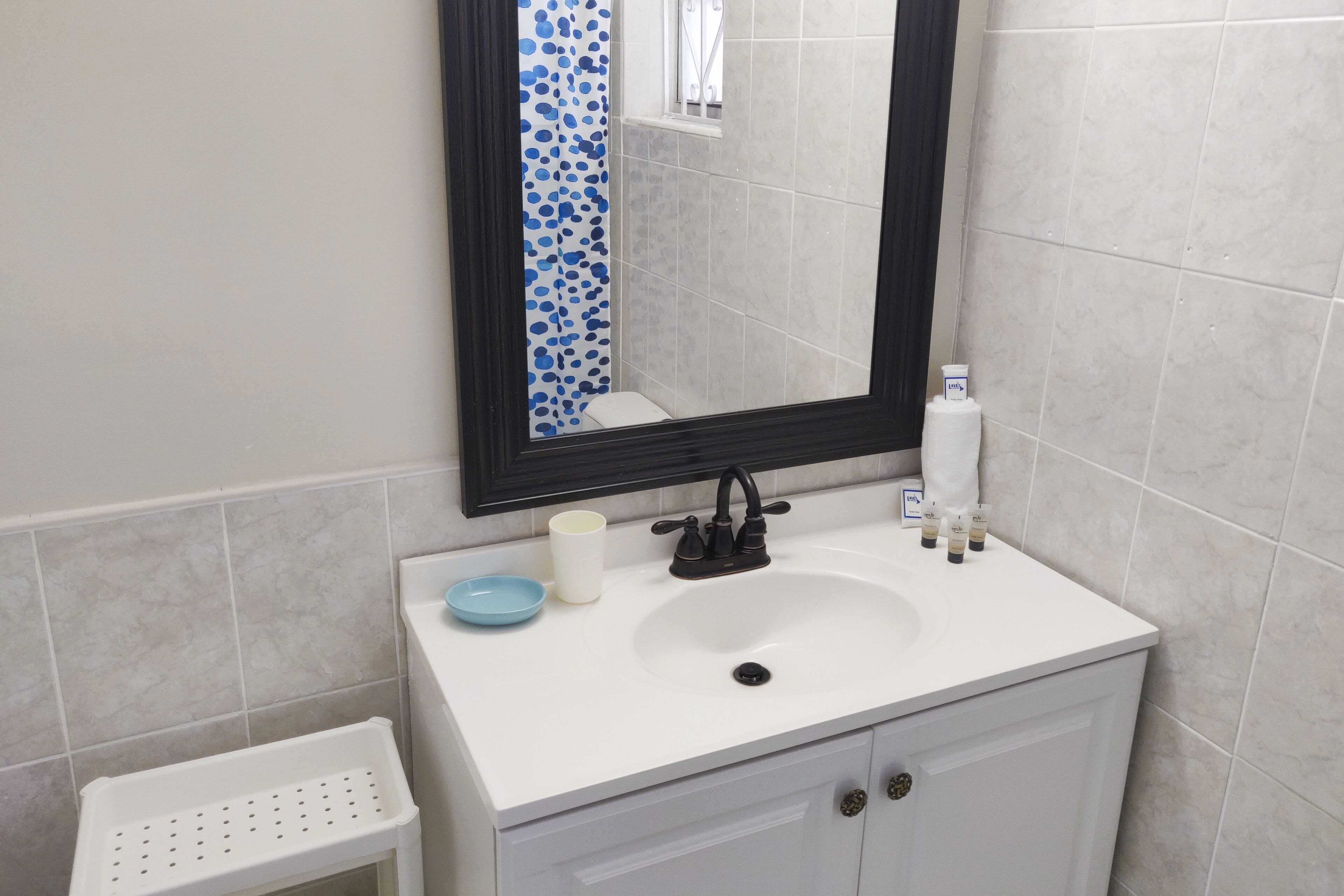 A bathroom with a white sink, a mirror, and a small white stool.