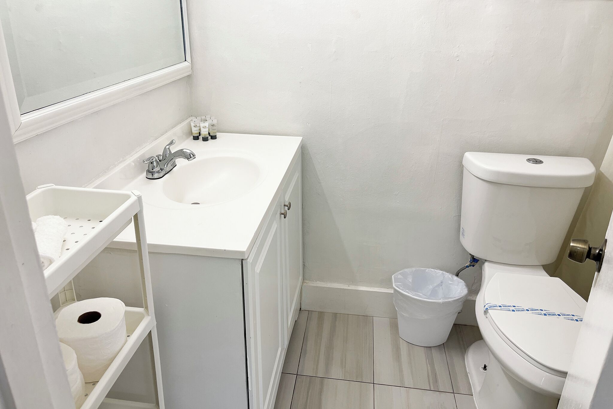 A bathroom with a white sink, toilet, and a small trash bin.