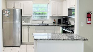 A kitchen with white cabinets, a stainless steel refrigerator, a microwave, a sink, and a fire extinguisher. - Sunny Isles Apartments by MiaRentals (Sunny Isles Beach)