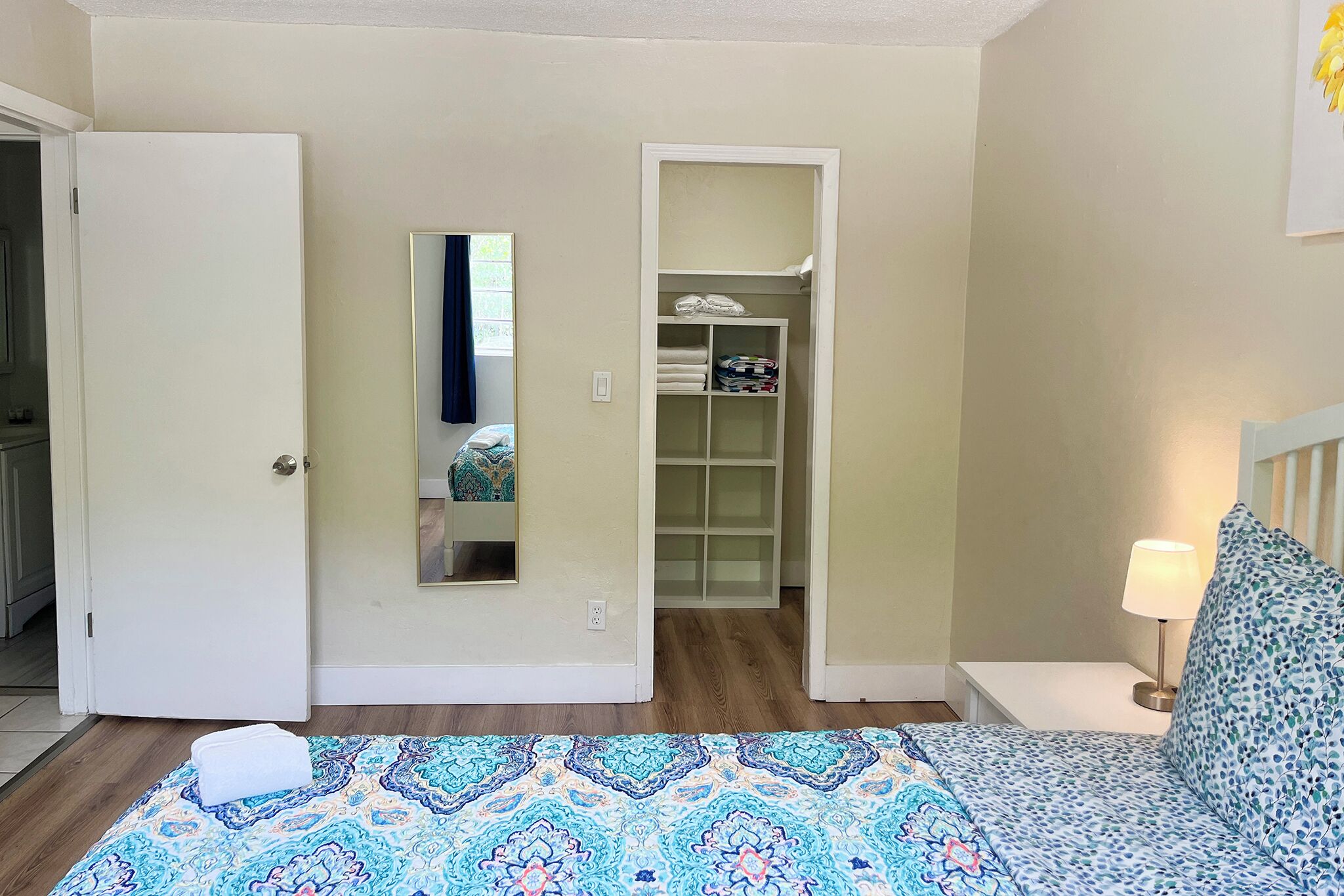 Une chambre à coucher comprenant un lit, une table de chevet avec une lampe, une armoire avec des étagères et une porte donnant sur une autre pièce.