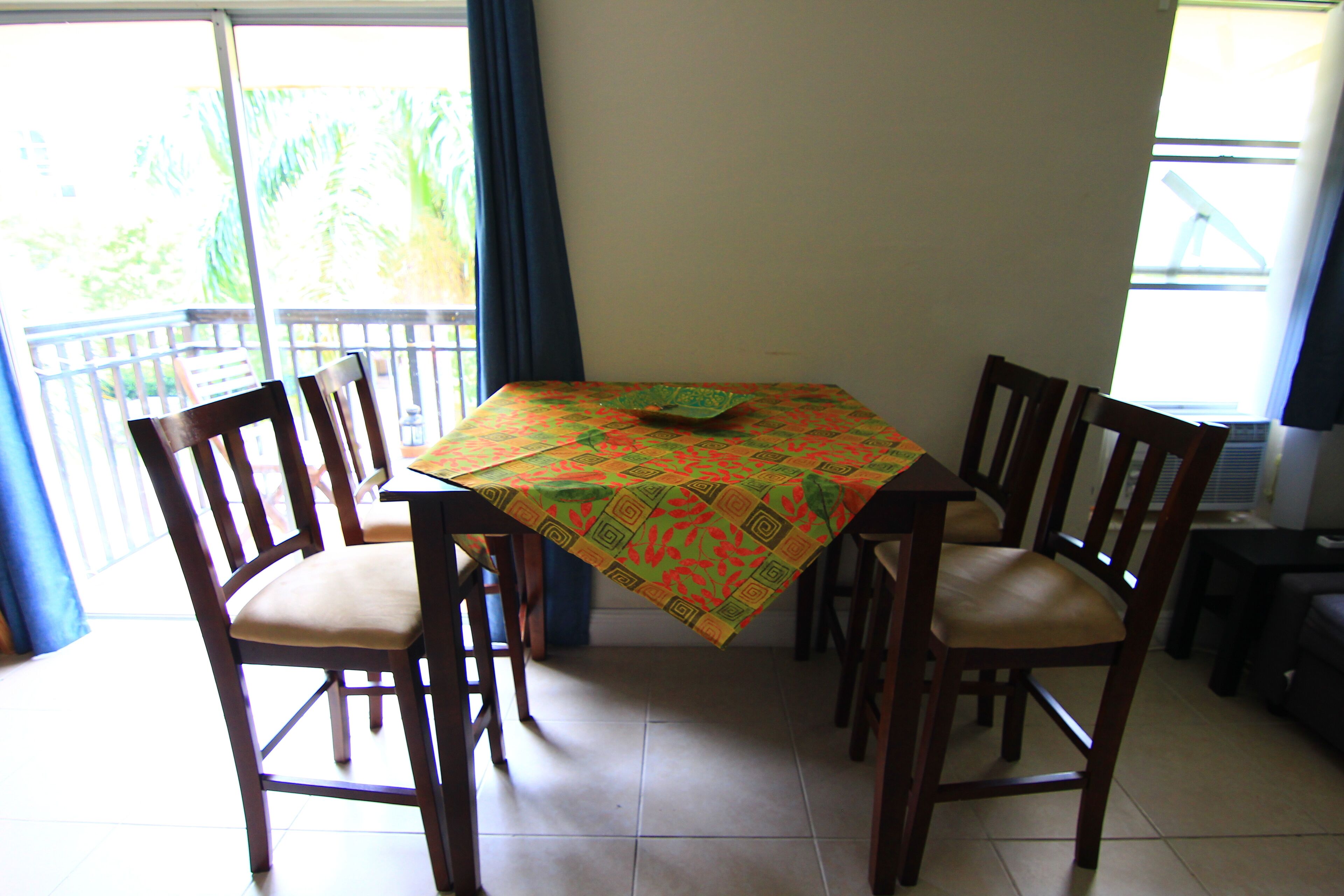A dining area with a table covered by a patterned tablecloth, surrounded by wooden chairs with cushioned seats.