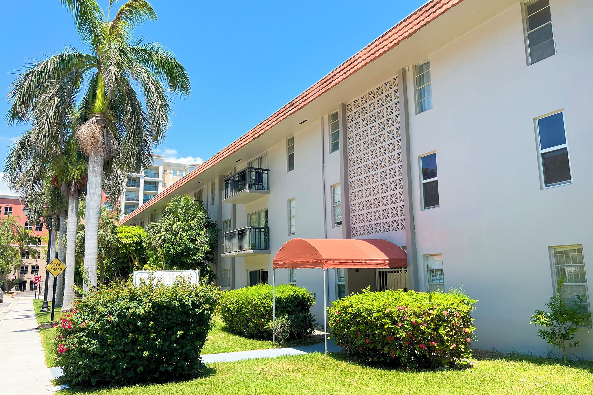 A multi-story building with balconies, a covered outdoor seating area, and lush greenery.
