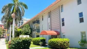A multi-story building with balconies, a covered outdoor seating area, and lush greenery.